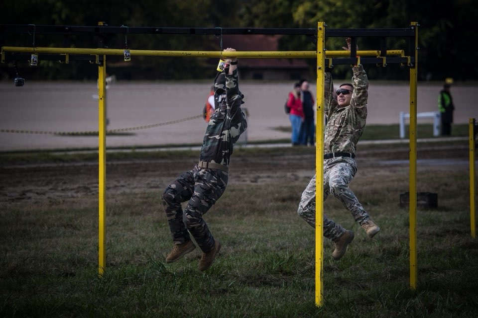 Participants in uniform climbing an outdoor obstacle course.