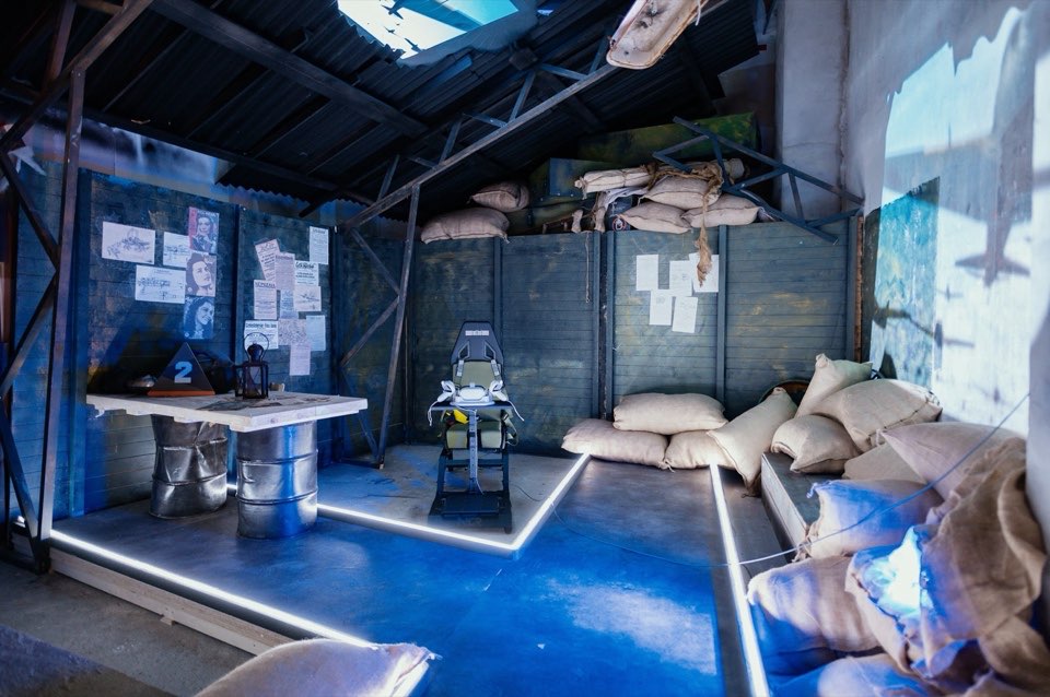 A bunker-style set with sandbags and a desk, lit in blue.