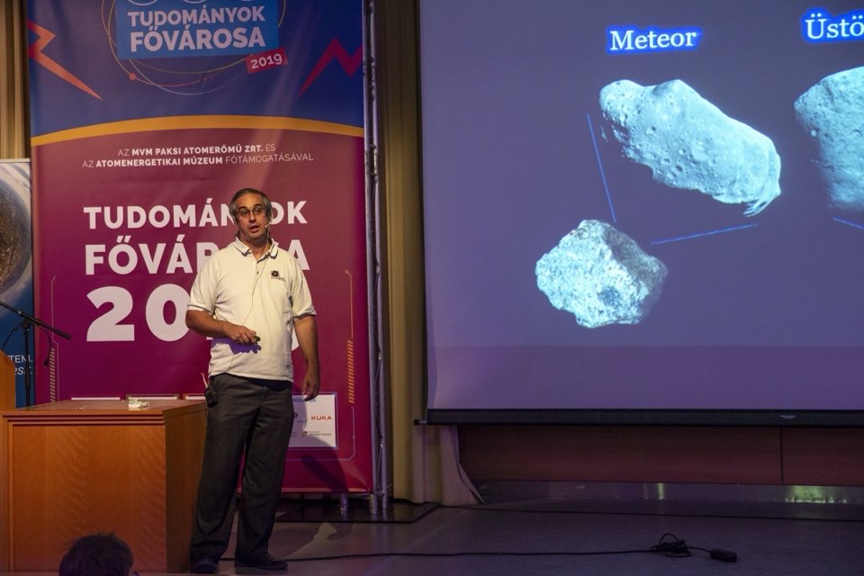 A speaker on stage in front of a projected slide showing meteorites.