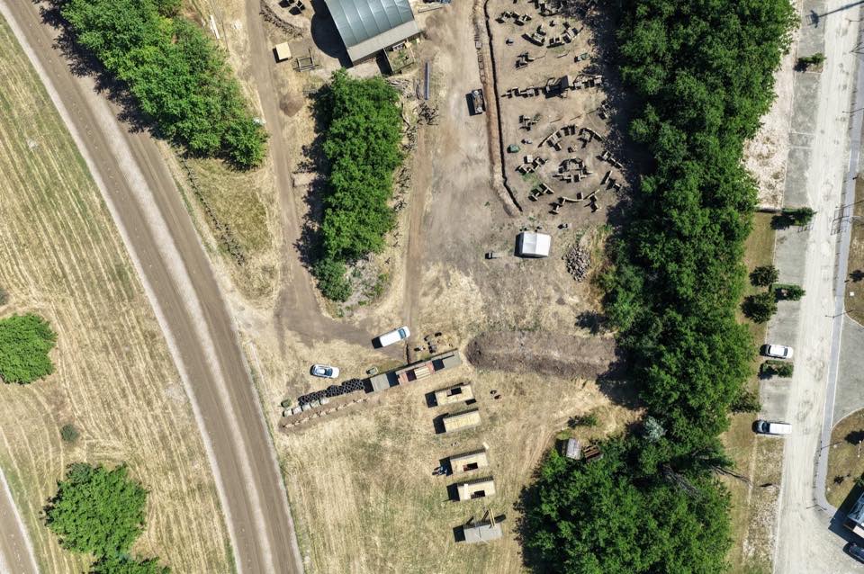 Aerial view of an outdoor site with a track, tree lines and parked vehicles.