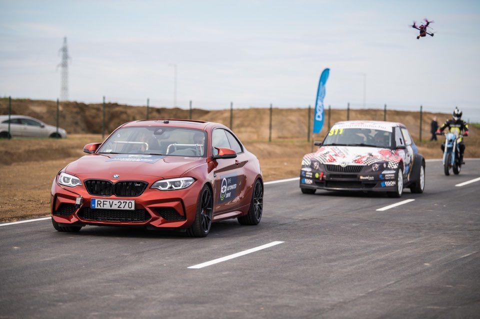 Two cars on a test track, with a drone filming overhead.